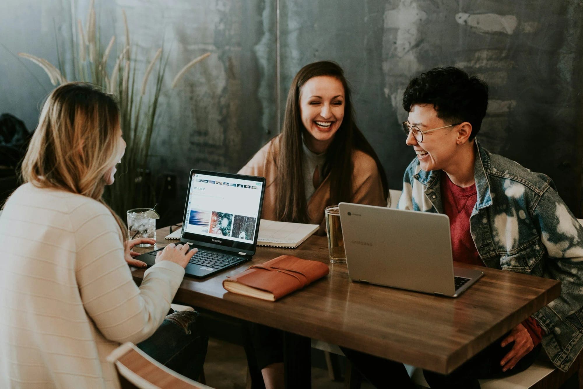 Three friends laughing together over laptops in a café