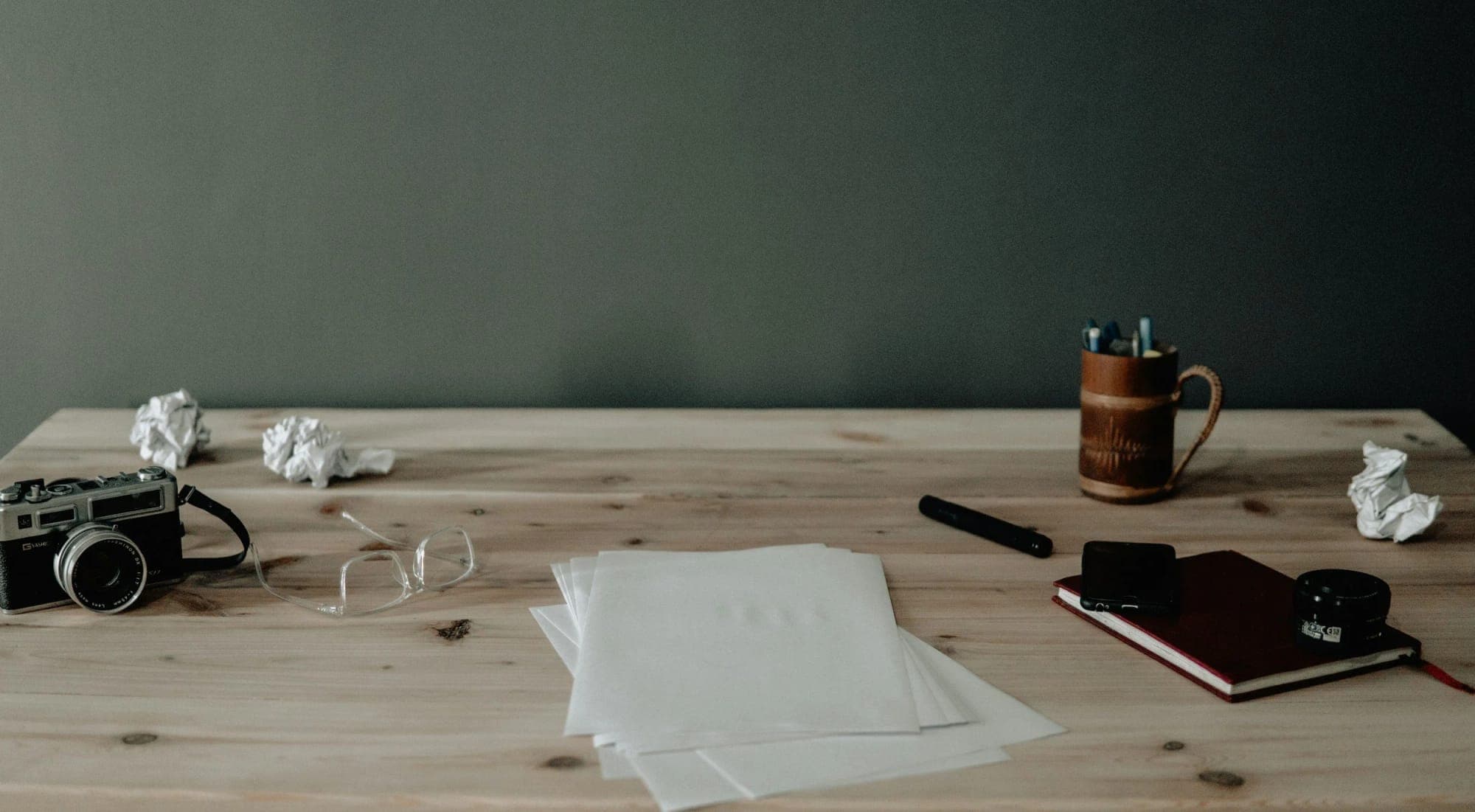 Empty desk with a camera, notebook and pen against a dark wall