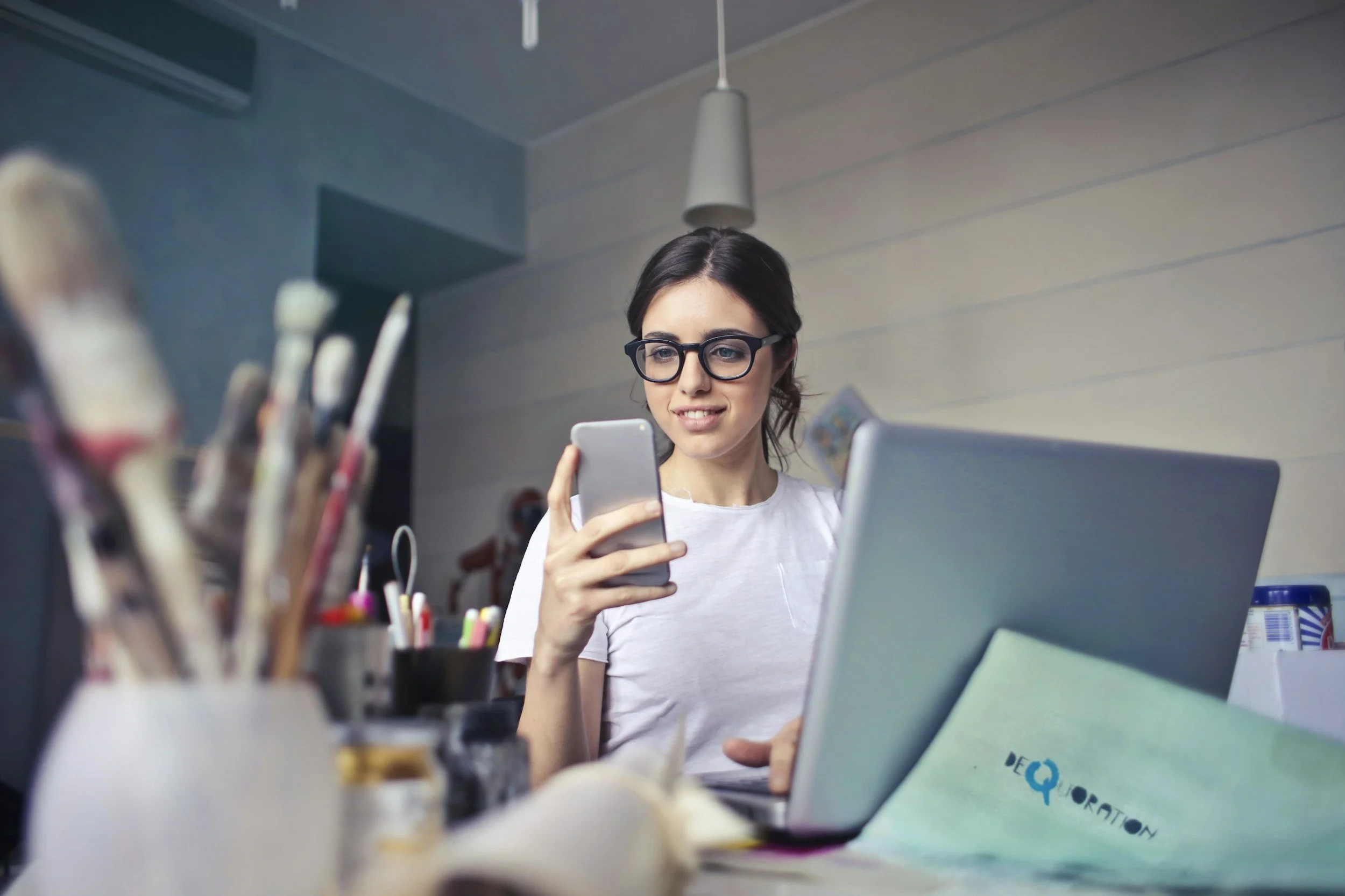 Woman smiling at her phone at a desk with a laptop