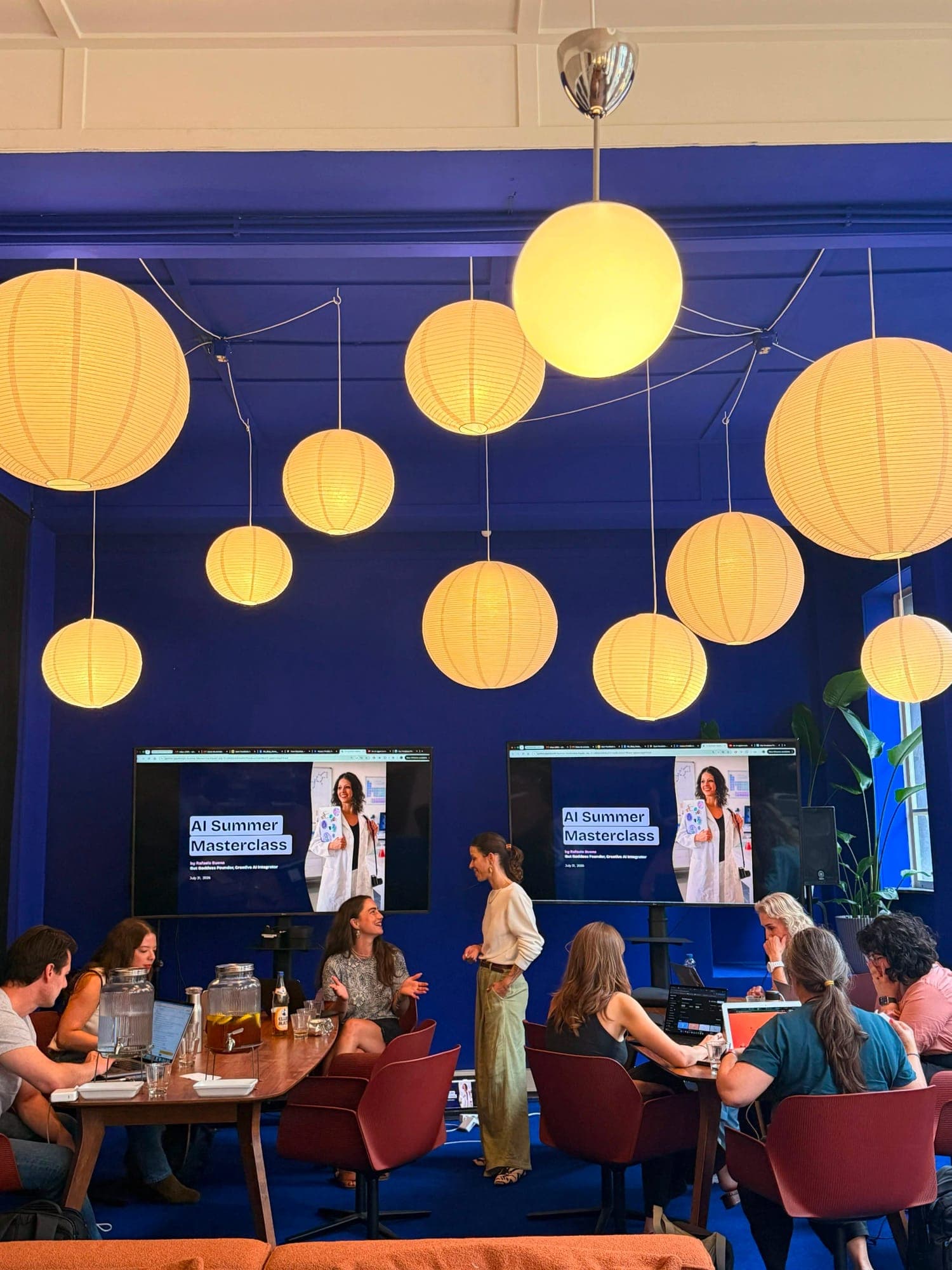 Rafaela Buena running an AI masterclass for a team in a blue room with paper lanterns in Amsterdam