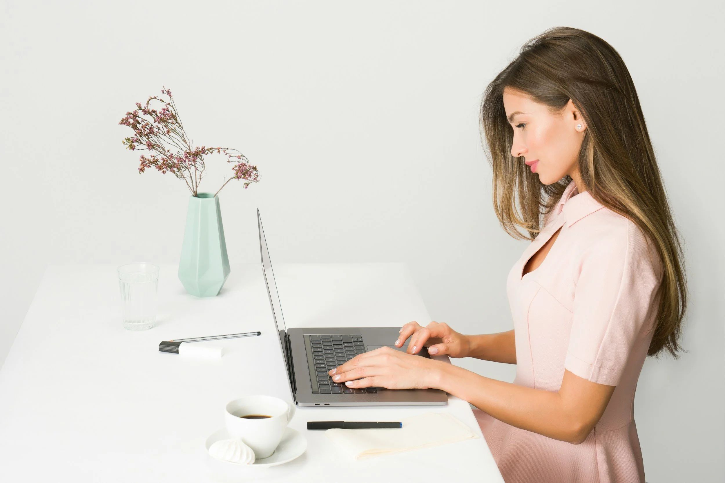 Woman typing on a laptop at a white desk