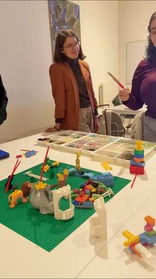 Participants at a table of LEGO® models, one holding up a red brick as she talks